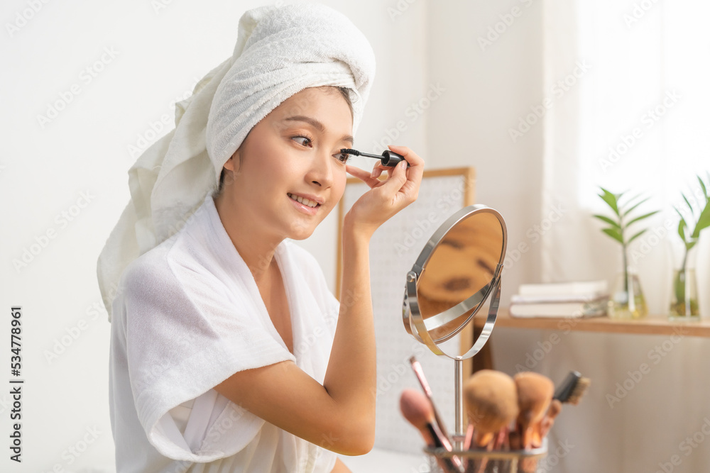 Happy beauty, cute asian young woman wearing bathrobe, make up face hand by applying mascara brush on eyelash, looking into mirror in morning routine at home. Person look with natural fashion style. Happy beauty, cute asian young woman wearing bathrobe, make up face hand by applying mascara brush on eyelash, looking into mirror in morning routine at home. Person look with natural fashion style.