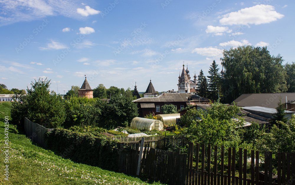 Beautiful rustic landscape with wooden houses and vegetable gardens with beds behind a fence among green trees on a sunny summer day against a blue clear sky in Yuriev-Polsky russia Beautiful rustic landscape with wooden houses and vegetable gardens with beds behind a fence among green trees on a sunny summer day against a blue clear sky in Yuriev-Polsky russia