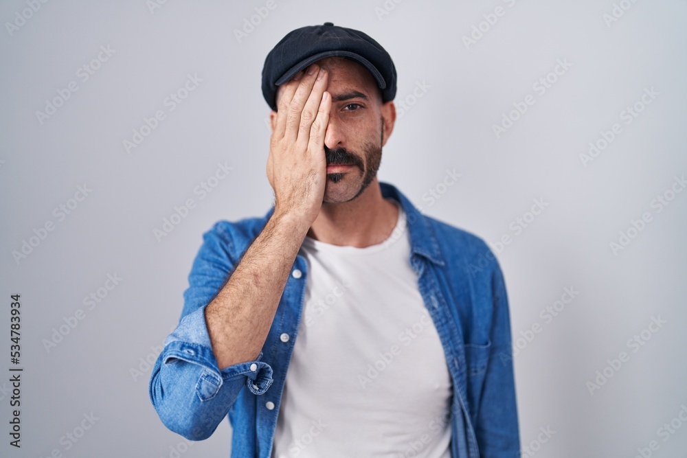 Hispanic man with beard standing over isolated background yawning tired covering half face, eye and mouth with hand. face hurts in pain. Hispanic man with beard standing over isolated background yawning tired covering half face, eye and mouth with hand. face hurts in pain.
