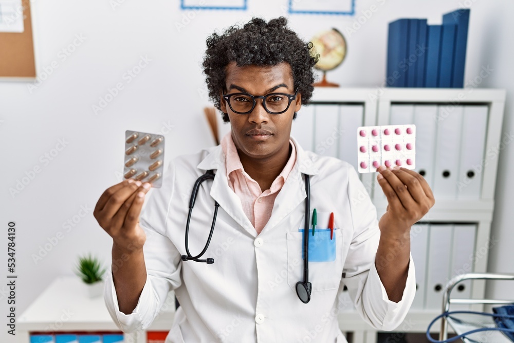 African man wearing doctor uniform holding prescription pills skeptic and nervous, frowning upset because of problem. negative person. African man wearing doctor uniform holding prescription pills skeptic and nervous, frowning upset because of problem. negative person.