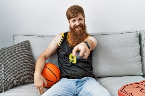 Young irish man smiling happy watching basketball game on tv at home.