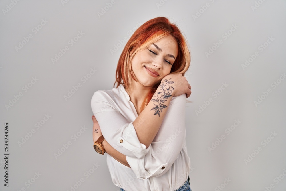 Young caucasian woman standing over isolated background hugging oneself happy and positive, smiling confident. self love and self care Young caucasian woman standing over isolated background hugging oneself happy and positive, smiling confident. self love and self care
