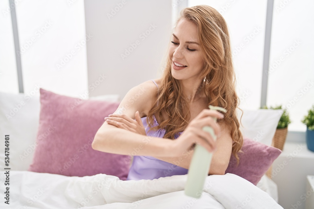 Young blonde woman applying skin lotion sitting on bed at bedroom Young blonde woman applying skin lotion sitting on bed at bedroom