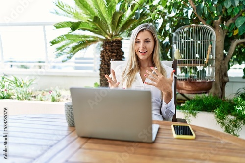 Young blonde woman having video call using laptop working at the terrace.