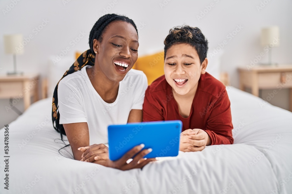 Obraz premium African american mother and son using touchpad lying on bed at bedroom