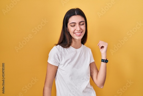 Young beautiful woman standing over yellow background dancing happy and cheerful, smiling moving casual and confident listening to music