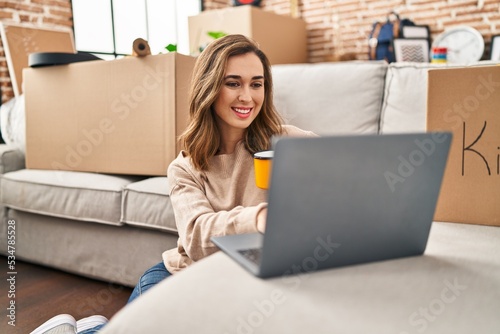 Young woman drinking coffee using laptop at new home