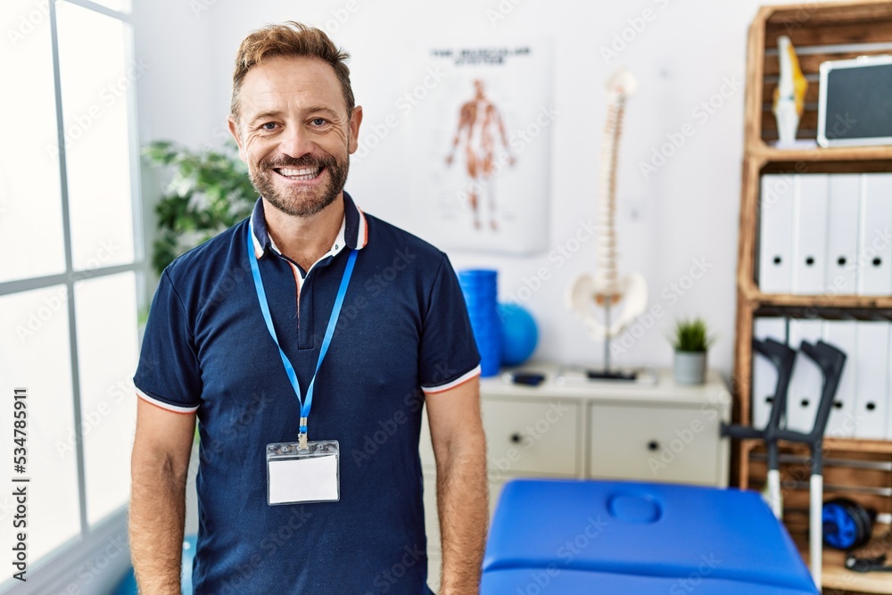 Middle age physiotherapist man working at pain recovery clinic with a happy and cool smile on face. lucky person. Middle age physiotherapist man working at pain recovery clinic with a happy and cool smile on face. lucky person.