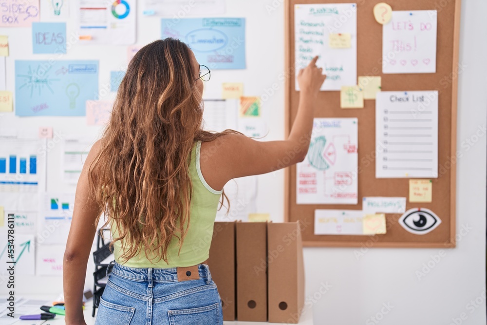 Young beautiful hispanic woman business worker looking and pointing at corkboard at office Young beautiful hispanic woman business worker looking and pointing at corkboard at office