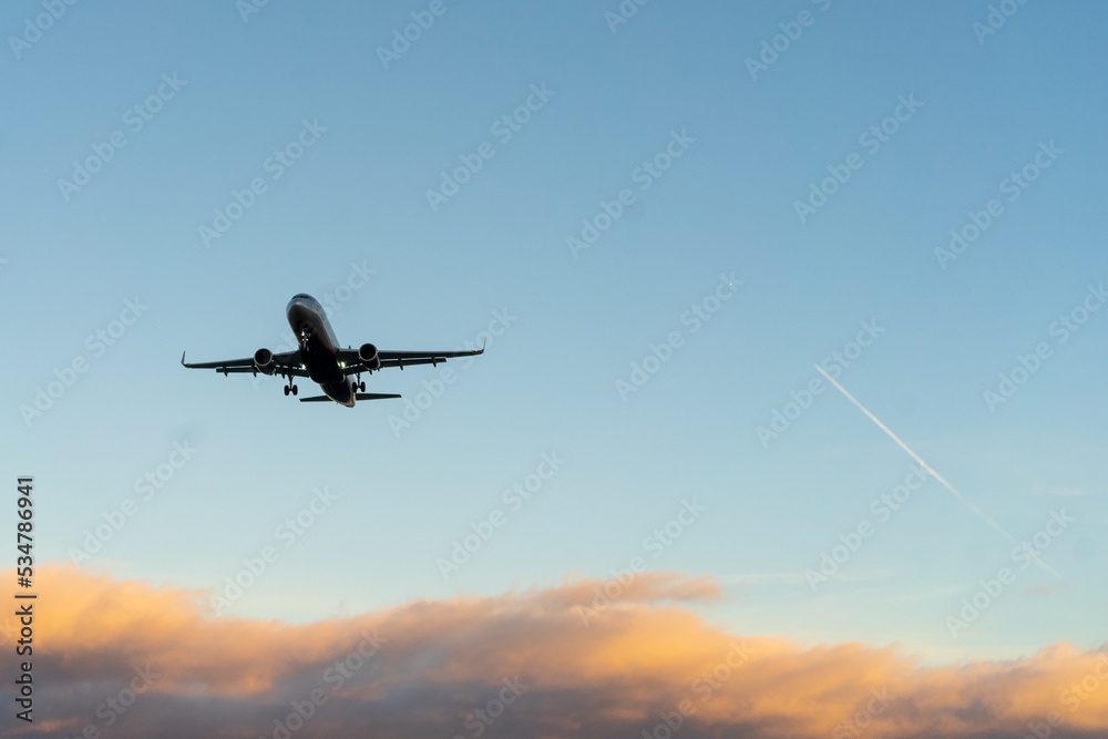 The silhouette of a passenger plane coming in for landing against the backdrop of the sunset sky.