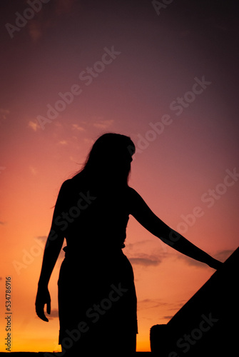 Silueta de una mujer al atardecer con cielo en tonos cálidos