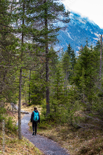 girl with a backpack walks along a road with huge clouded mountain peaks in the background  Swiss alps, hiking to Lake Oeschinen  © Jakub