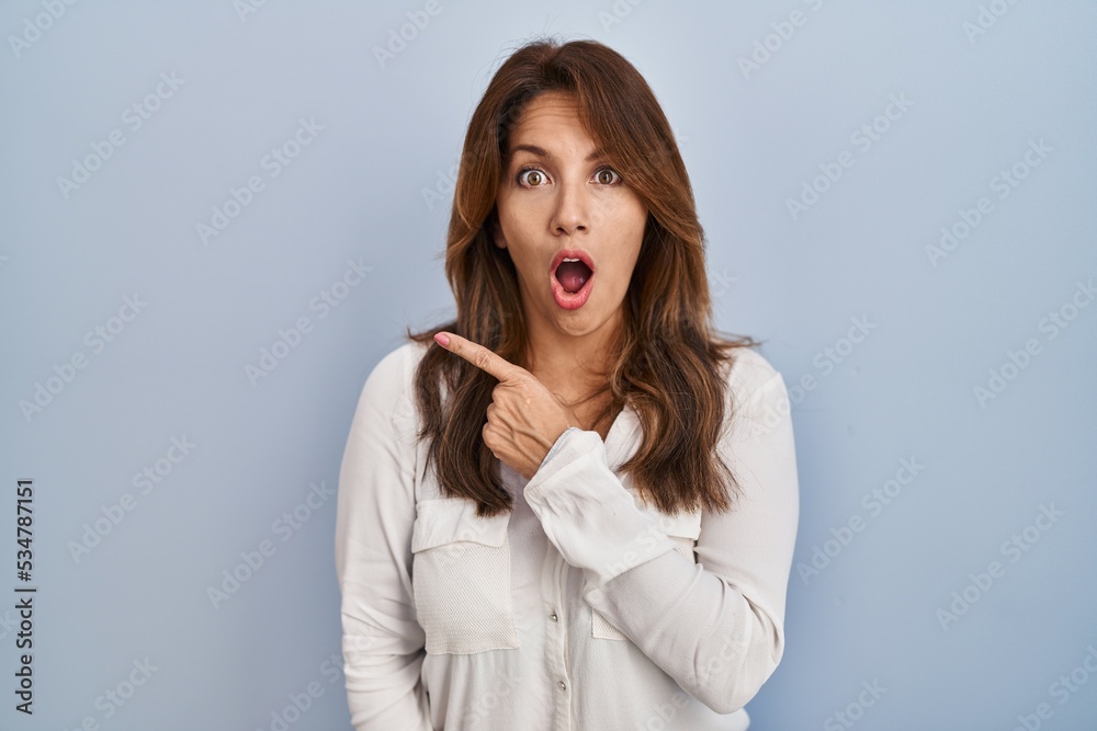 Hispanic woman standing over isolated background surprised pointing with finger to the side, open mouth amazed expression. Hispanic woman standing over isolated background surprised pointing with finger to the side, open mouth amazed expression.