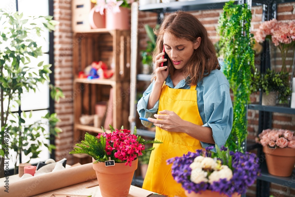 Young beautiful hispanic woman florist talking on smartphone using touchpad at florist
