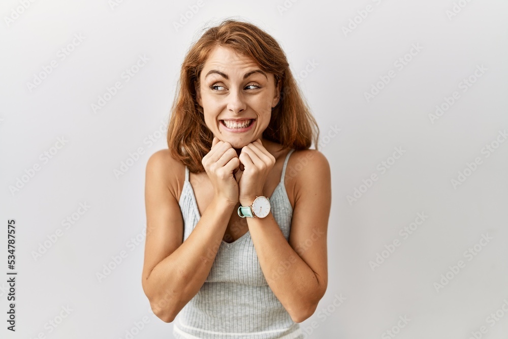 Beautiful caucasian woman standing over isolated background laughing nervous and excited with hands on chin looking to the side Beautiful caucasian woman standing over isolated background laughing nervous and excited with hands on chin looking to the side