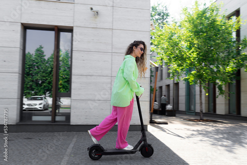 Attractive smiling woman riding electric kick scooter at beautiful cityscape.Eco friendly transport photo