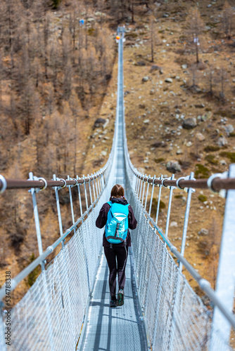 Girl in pigtails walks across the longest suspension bridge in the world - Charles Kuonen Suspension Bridge  walk across the fearsome bridge overlooking the mighty snowy alpine peaks, switzerland © Jakub