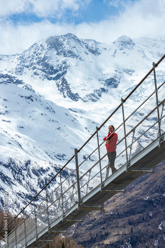 Girl in pigtails walks across the longest suspension bridge in the world - Charles Kuonen Suspension Bridge; walk across the fearsome bridge overlooking the mighty snowy alpine peaks, switzerland
