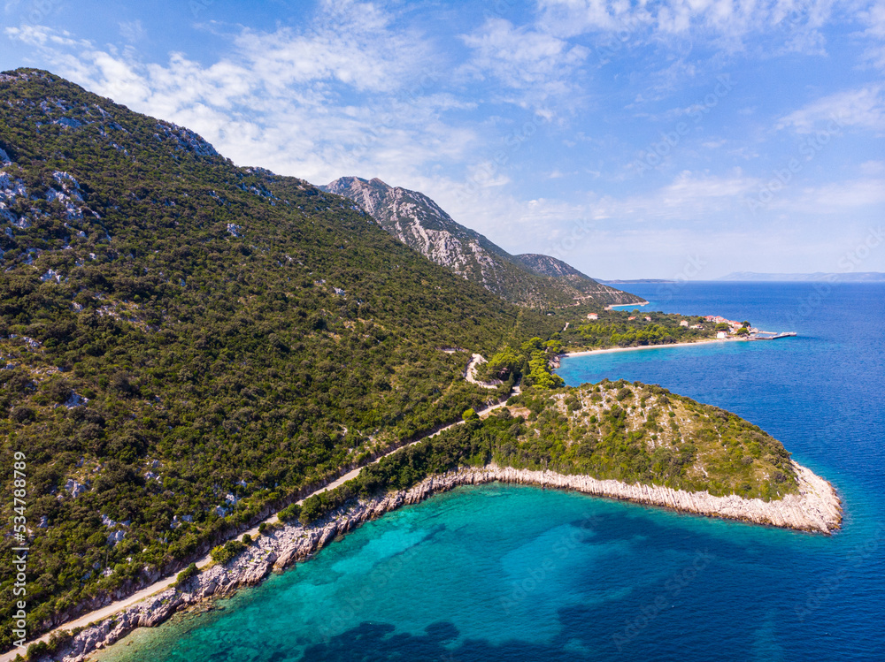 aerial view of a paradisiacal Mediterranean bay with turquoise water surrounded by massive mountains, with floating motorboats, with a small bushy island; the bay on the peljesac peninsula seen from a