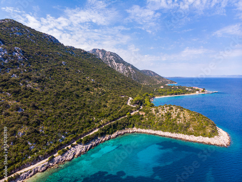 aerial view of a paradisiacal Mediterranean bay with turquoise water surrounded by massive mountains, with floating motorboats, with a small bushy island  the bay on the peljesac peninsula seen from a © Jakub
