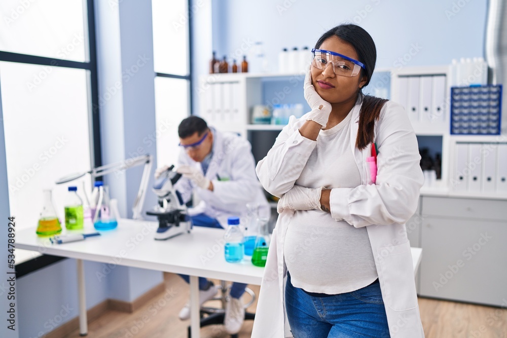 Young hispanic woman expecting a baby working at scientist laboratory thinking looking tired and bored with depression problems with crossed arms. Young hispanic woman expecting a baby working at scientist laboratory thinking looking tired and bored with depression problems with crossed arms.