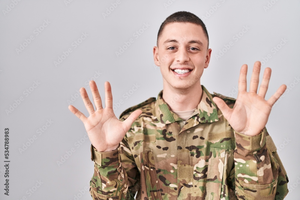 Young man wearing camouflage army uniform showing and pointing up with fingers number ten while smiling confident and happy. Young man wearing camouflage army uniform showing and pointing up with fingers number ten while smiling confident and happy.