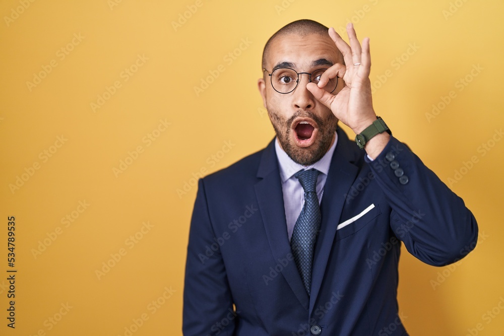 Hispanic man with beard wearing suit and tie doing ok gesture shocked with surprised face, eye looking through fingers. unbelieving expression. Hispanic man with beard wearing suit and tie doing ok gesture shocked with surprised face, eye looking through fingers. unbelieving expression.