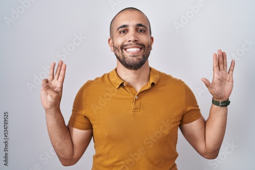 Hispanic man with beard standing over white background showing and pointing up with fingers number eight while smiling confident and happy.