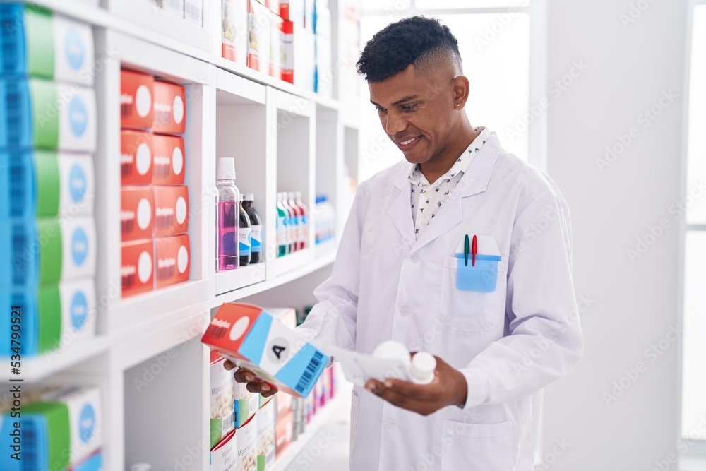 Young latin man pharmacist holding pills bottle reading prescription at pharmacy
