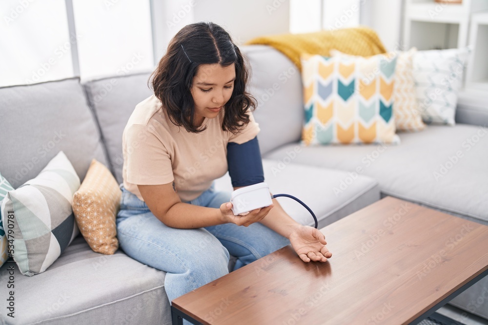 Young woman using tensiometer sitting on sofa at home Young woman using tensiometer sitting on sofa at home