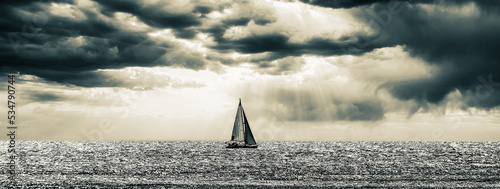 Black and white photo of a sailing boat on the sea in a dramatic sunset 