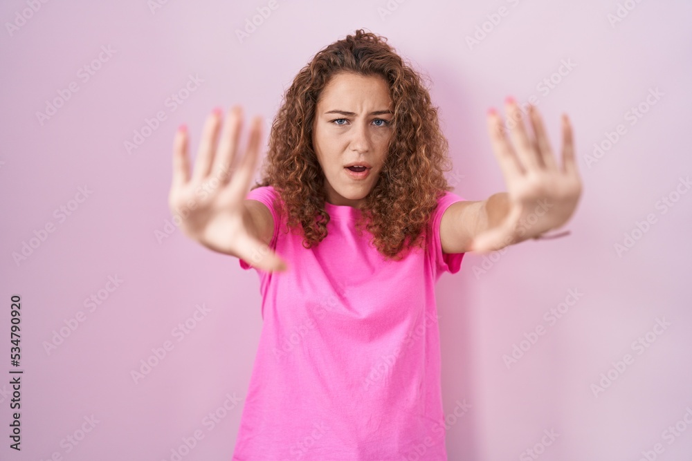 Young caucasian woman standing over pink background doing stop gesture with hands palms, angry and frustration expression Young caucasian woman standing over pink background doing stop gesture with hands palms, angry and frustration expression