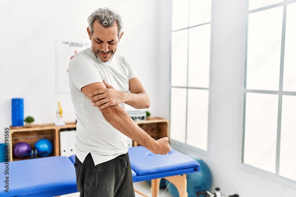 Middle age grey-haired man patient suffering for arm pain standing at rehab clinic