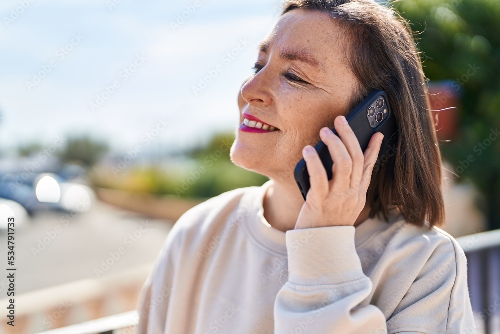 Middle age woman smiling confident talking on the smartphone at park