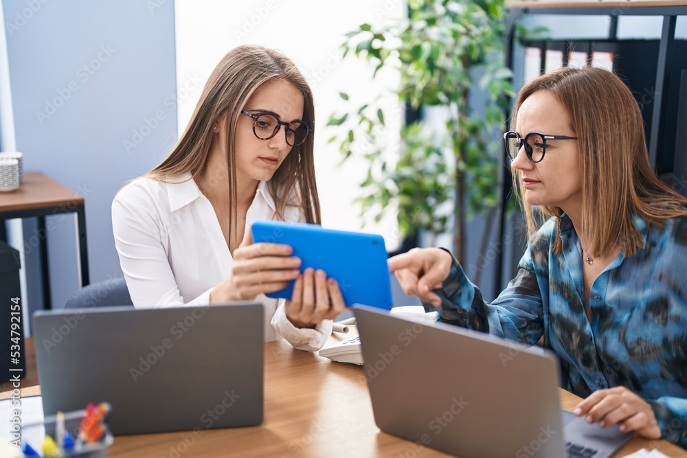 Two women business workers using laptop and touchpad working at office Two women business workers using laptop and touchpad working at office