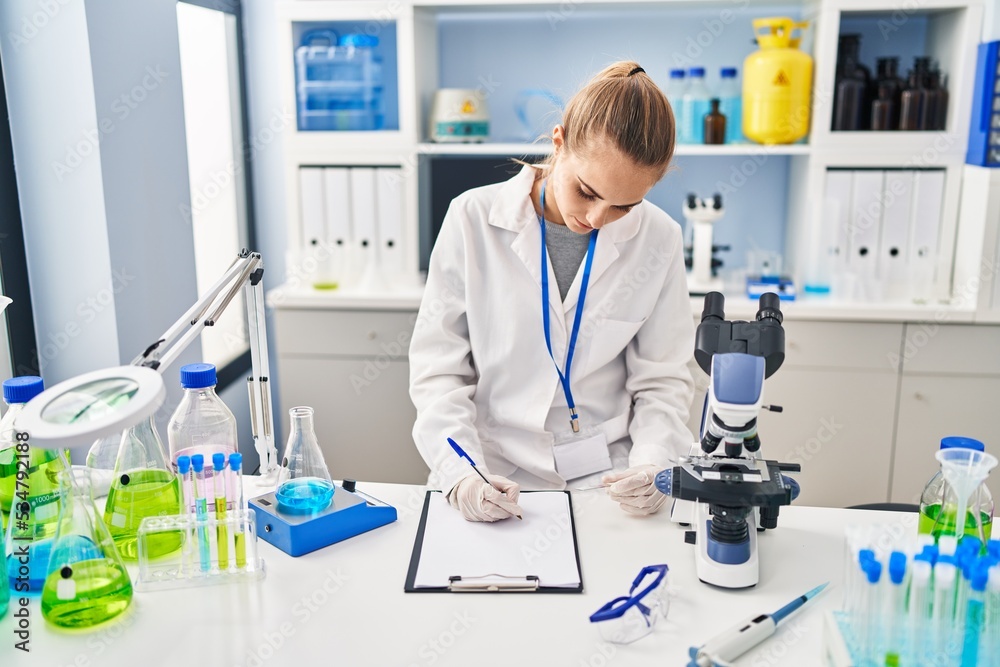 Young blonde woman wearing scientist uniform writing on checklist at laboratory Young blonde woman wearing scientist uniform writing on checklist at laboratory