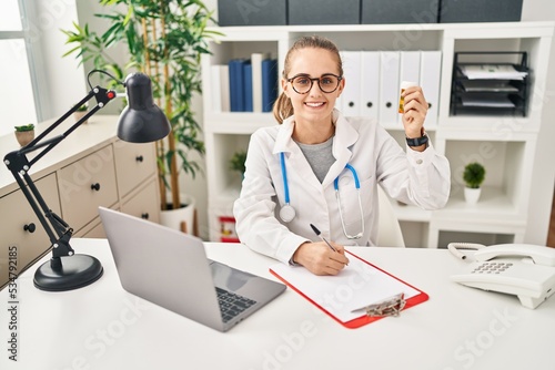 Young blonde woman wearing doctor uniform prescribe pills at clinic