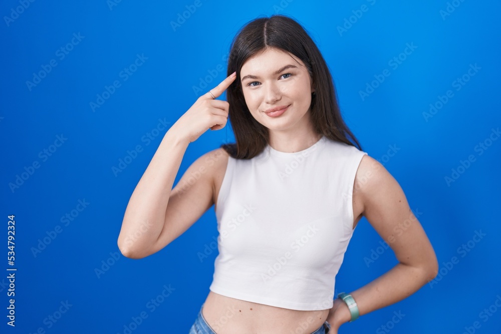 Young caucasian woman standing over blue background smiling pointing to head with one finger, great idea or thought, good memory