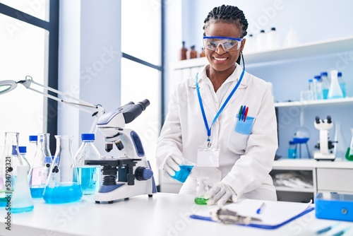 African american woman scientist smiling confident pouring liquid on test tube at laboratory