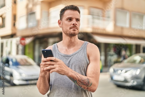 Young hispanic man using smartphone with serious expression at street