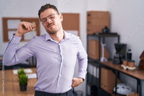 Young hispanic man at the office stretching back, tired and relaxed, sleepy and yawning for early morning