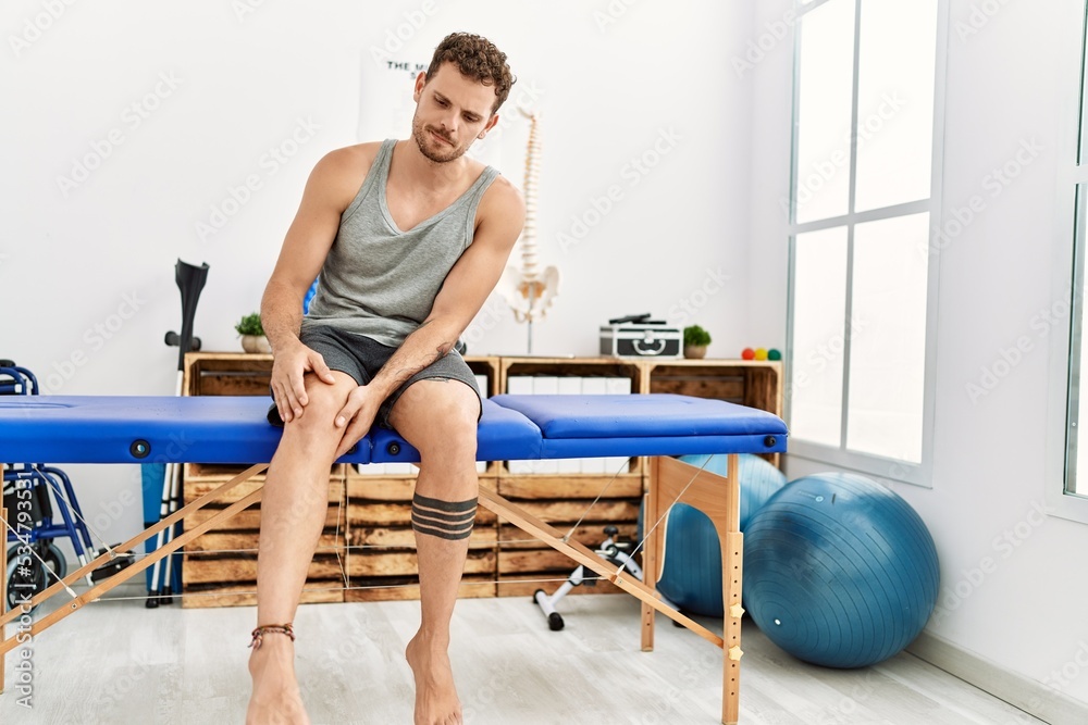 Obraz premium Young hispanic man suffering for knee pain sitting on massage board at clinic