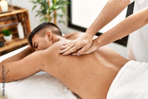 Young hispanic man relaxed having back massage at beauty center