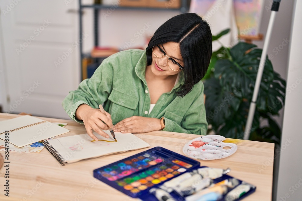 Young chinese woman artist smiling confident drawing on notebook at art studio
