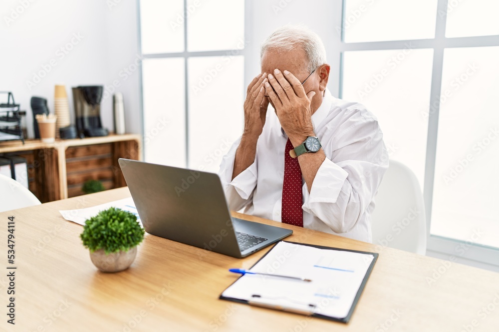 Senior man working at the office using computer laptop with sad expression covering face with hands while crying. depression concept. Senior man working at the office using computer laptop with sad expression covering face with hands while crying. depression concept.