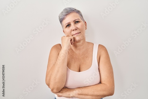 Middle age caucasian woman standing over white background with hand on chin thinking about question, pensive expression. smiling with thoughtful face. doubt concept.