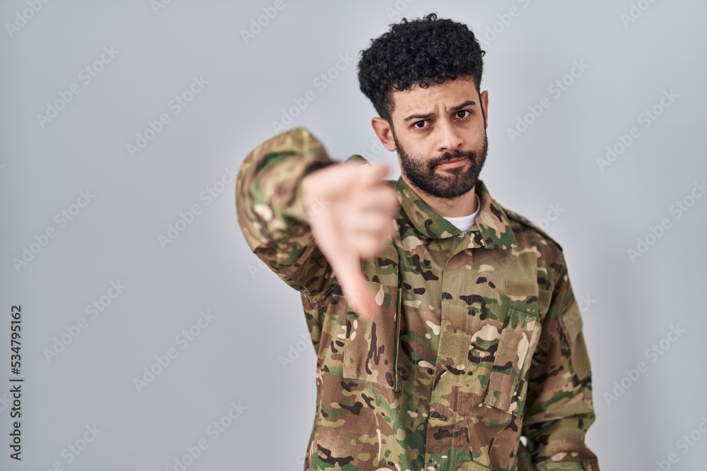 Arab man wearing camouflage army uniform looking unhappy and angry showing rejection and negative with thumbs down gesture. bad expression.