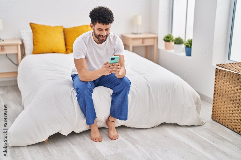 Young arab man using smartphone sitting on bed at bedroom Young arab man using smartphone sitting on bed at bedroom