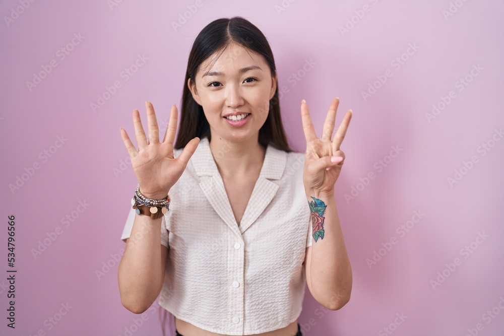 Chinese young woman standing over pink background showing and pointing up with fingers number eight while smiling confident and happy. Chinese young woman standing over pink background showing and pointing up with fingers number eight while smiling confident and happy.