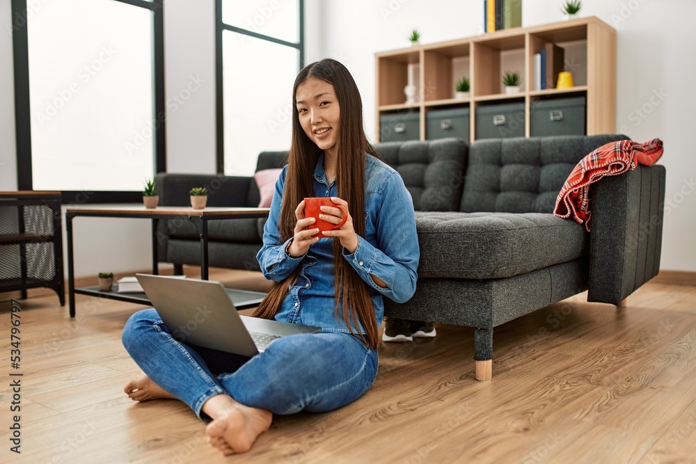 Young chinese girl using laptop and drinking coffee sitting on the ...